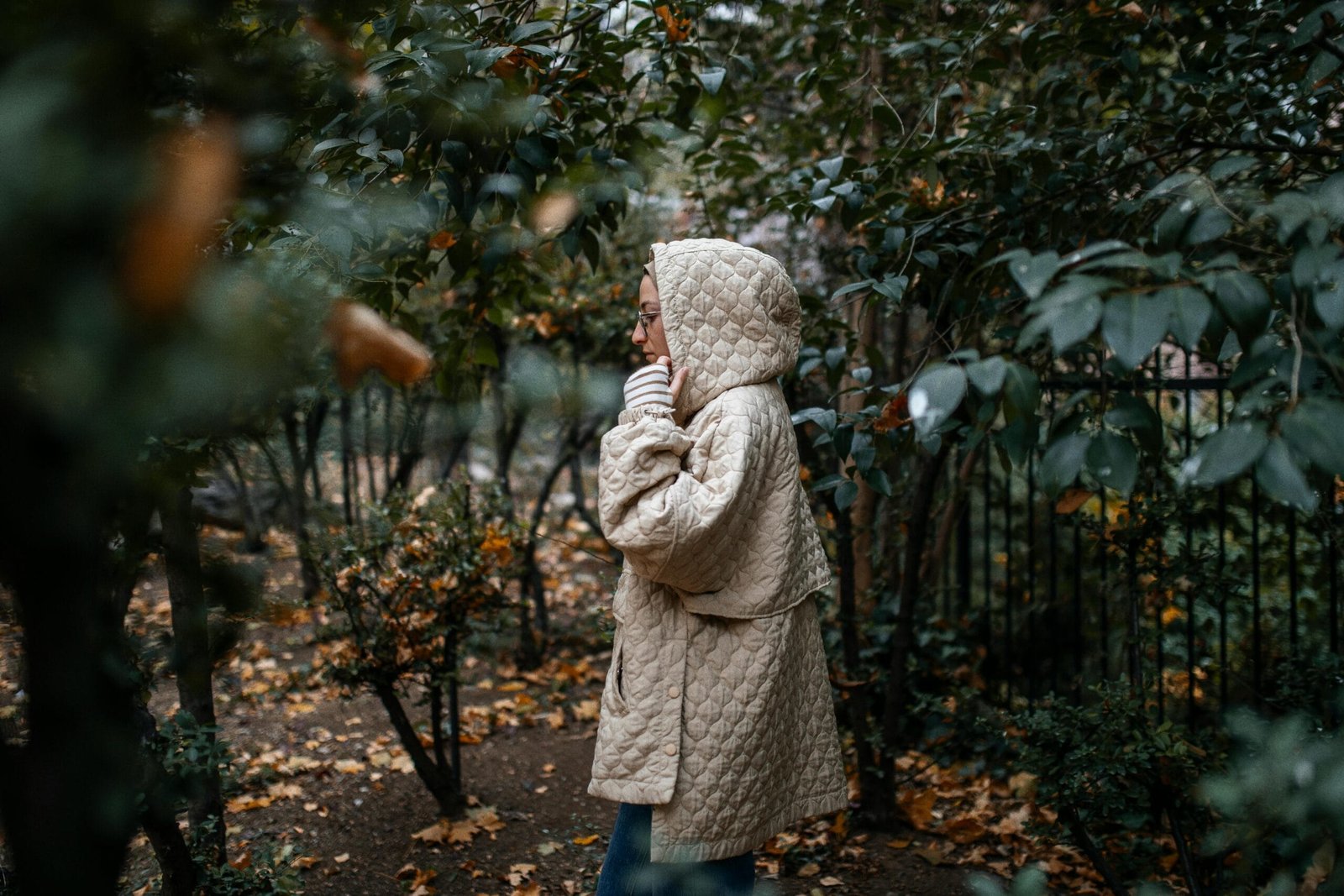 A woman in a quilted coat walks through an autumn orchard, surrounded by trees.
