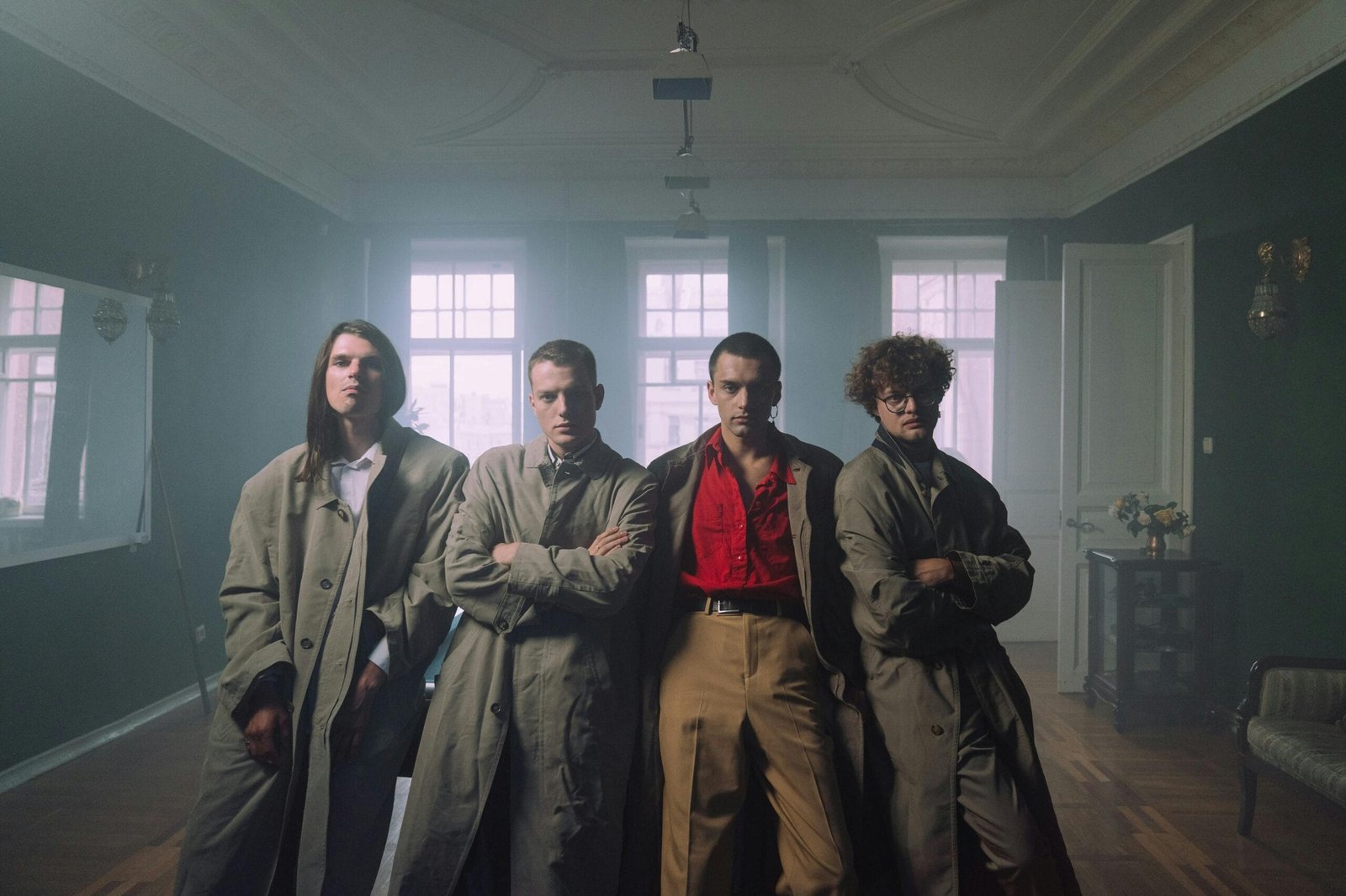 Four men in stylish trench coats pose confidently indoors, highlighting vintage fashion.