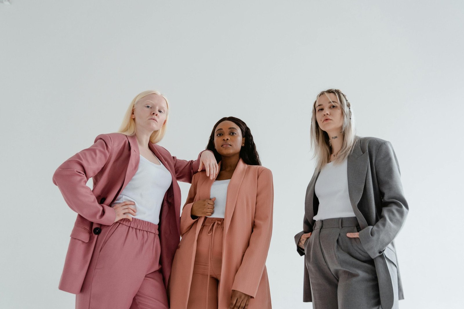 Three diverse women posing confidently in fashion-forward blazers against a white background.