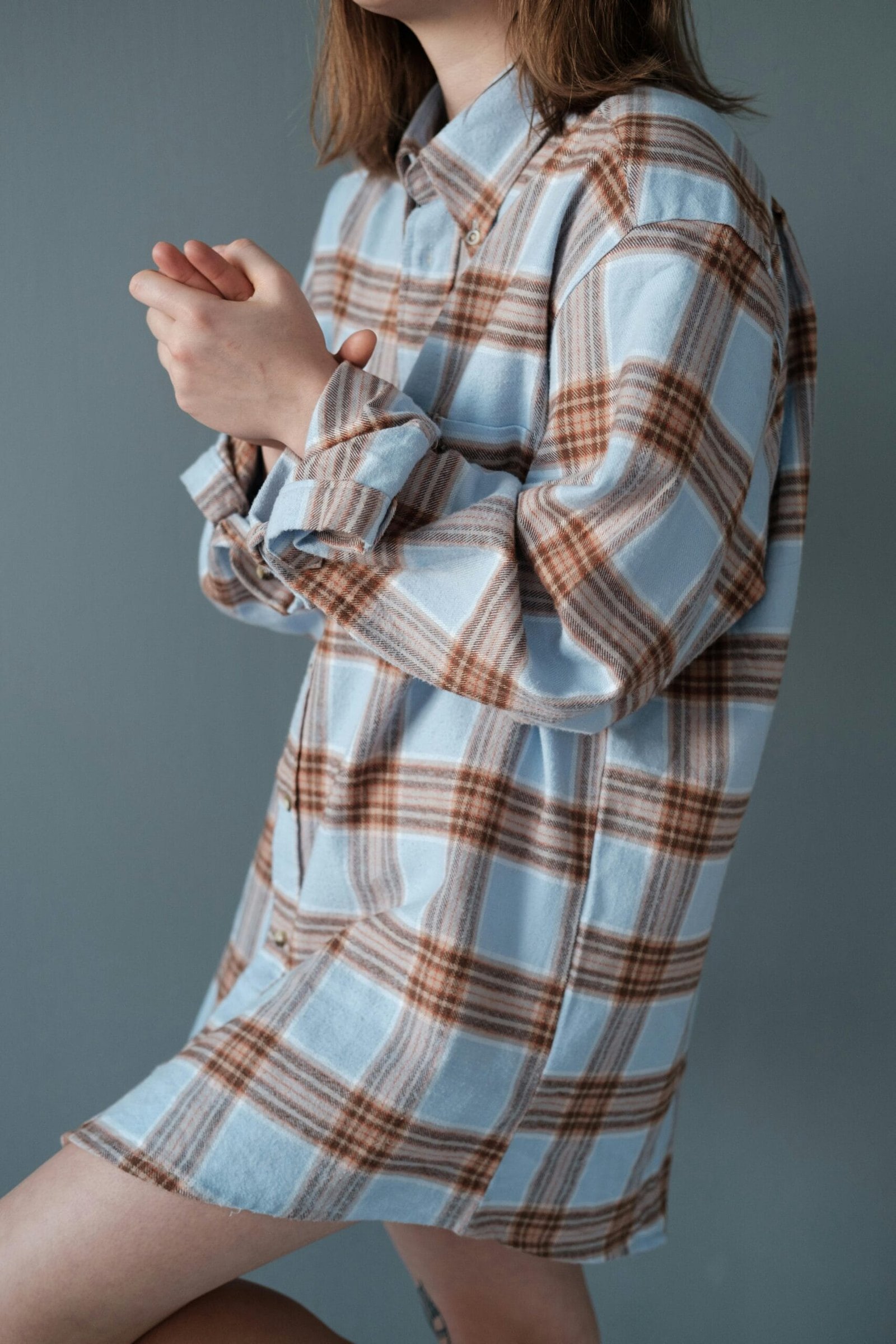 Portrait of a young woman wearing an oversized plaid shirt in a relaxed pose against a simple background.
